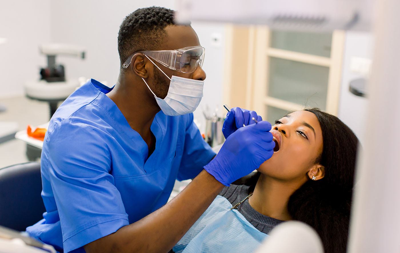Male african dentist examining a patient with tools in dental clinic. African female patient getting dental treatment in dental clinic